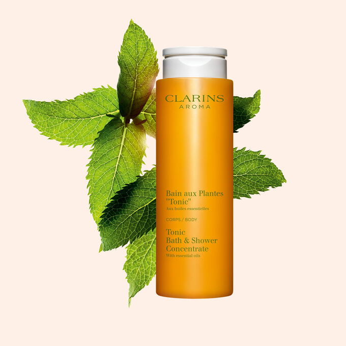 Packshot of Clarins Tonic Bath and Shower Concentrate gel, close to some mint and rosemary leaves on a orange background.