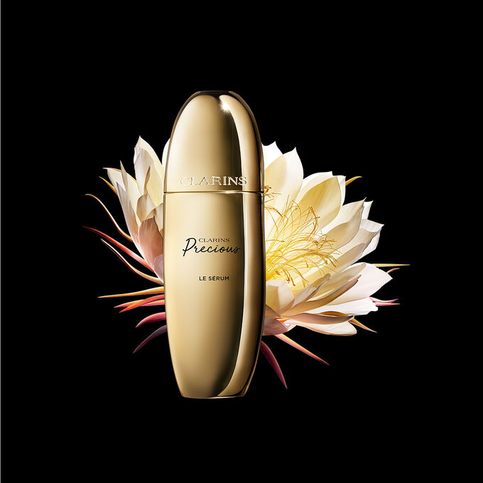 深色背景中的Clarins Precious至臻凝時精華的宣傳照，旁邊有一朵月神花。