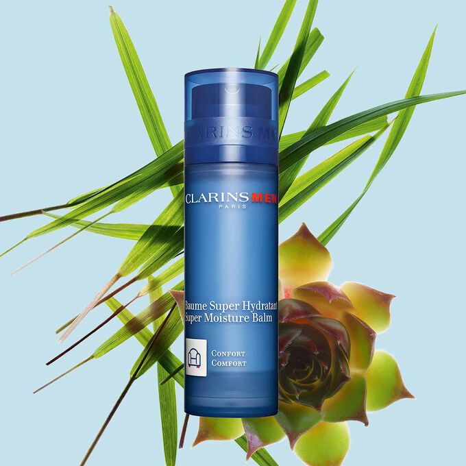 Packshot of a pump bottle of ClarinsMen Super Moisture Balm close to gymnena and bison grass on a blue background.