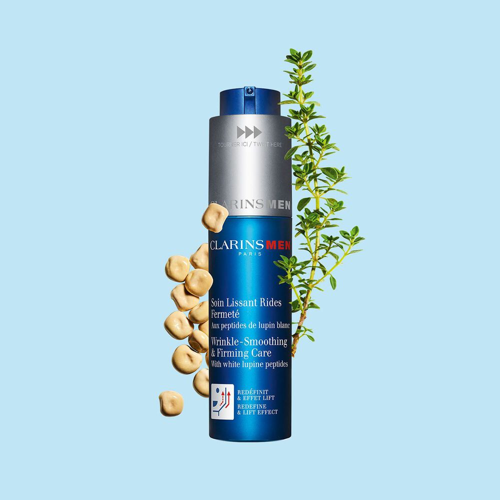 Packshot of the men's anti-aging care by Clarins next to white lupines on a light blue background to emphasize its key ingredient.