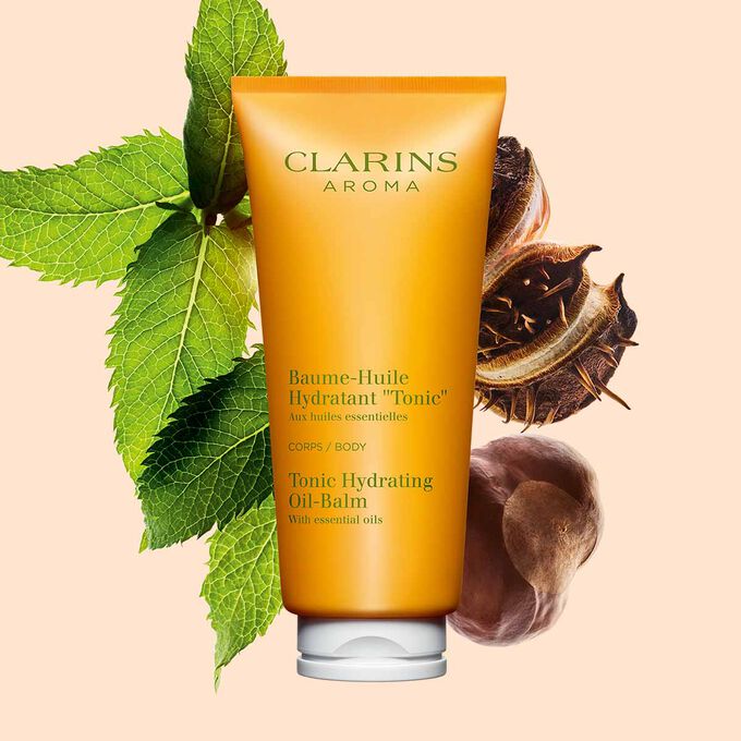 Packshot of a tube of Clarins Tonic Hydrating Oil-balm, close to some mint leaves and shea seeds on a peach background.