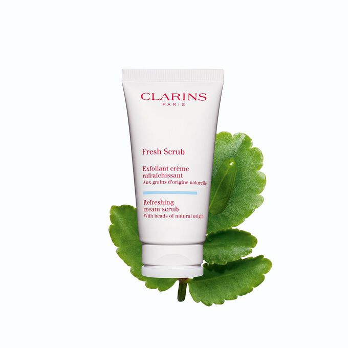 Packshot of Clarins face exfoliant Fresh Scrub tube next to some leaves of life on a white background.