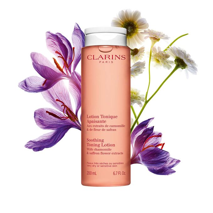 Packshot of the face lotion orange bottle next to a saffron flower and chamomile on a light orange background