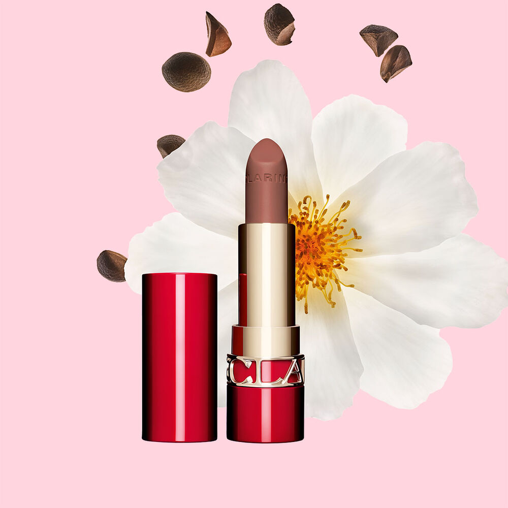 Packshot of Clarins matte Lipstick Joli Rouge in Shade 758 V, placed beside a camellia flower and shea seeds on a pink background.