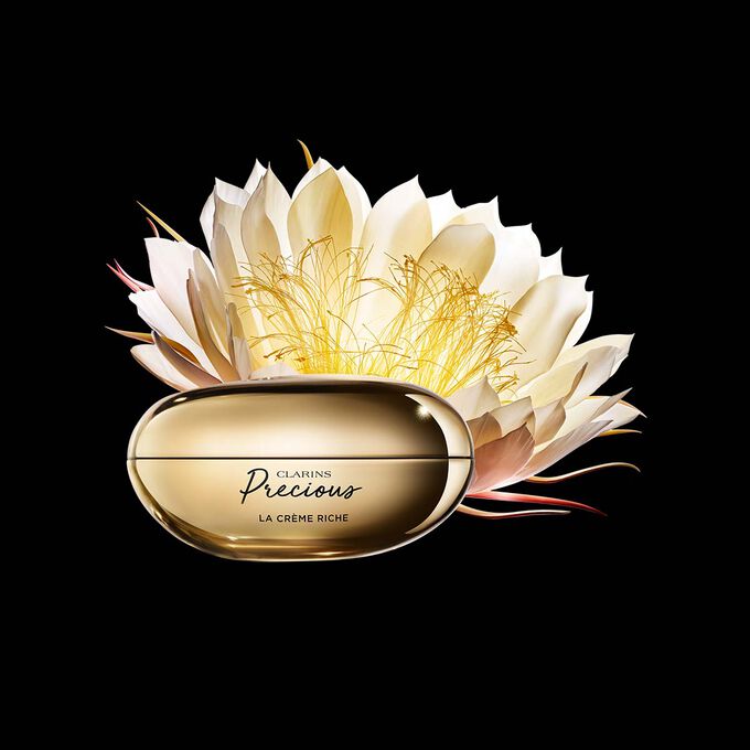 深色背景中的Clarins Precious至臻凝時面霜（滋潤型）的宣傳照，旁邊有一朵月神花。