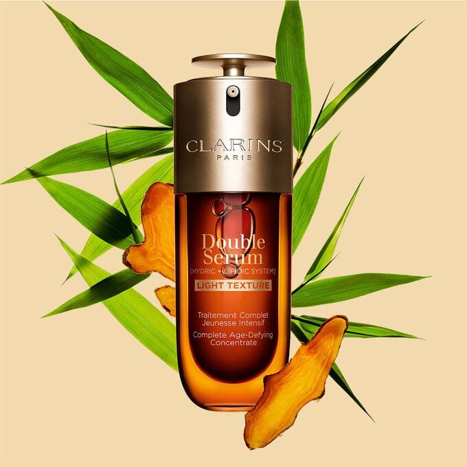 A 70ml bottle of Clarins Double Serum Light Texture among turmeric and proven&ccedil;al reed leaves against an orange background.