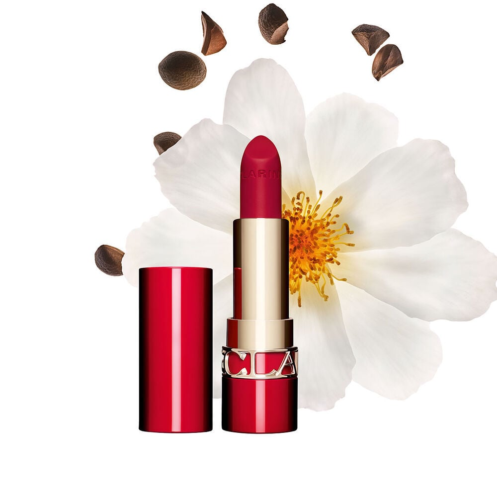Packshot of Clarins matte Lipstick Joli Rouge in Shade 742 V, placed beside a camellia flower and shea seeds on a pink background.