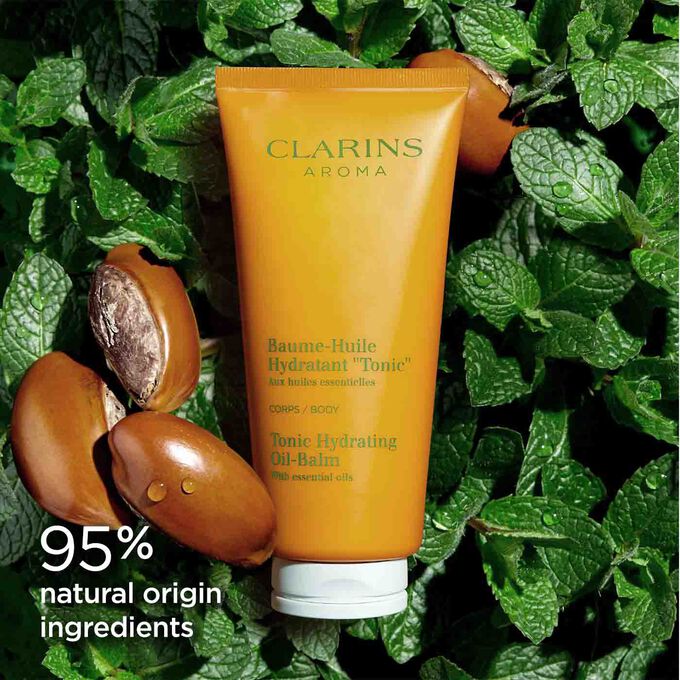 Tube of Clarins Tonic Hydrating Oil-balm among mint leaves and shea seeds to illustrate the natural origin of its ingredients