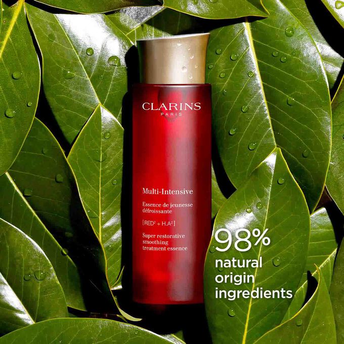 Packshot of Clarins Super Restorative Treatment Essence among Harungana leaves, highlighting 98% natural origin ingredients.