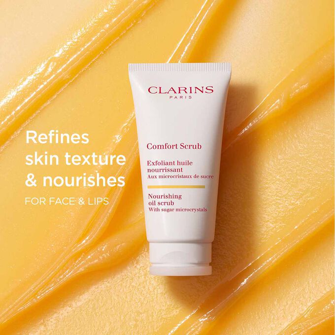 Clarins Comfort Scrub for the face and lips on an orange textured background to emphasize its refining and nourishing actions.