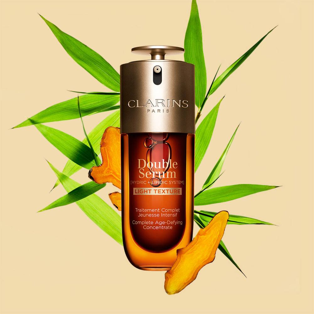 A 70ml bottle of Clarins Double Serum Light Texture among turmeric and provençal reed leaves against an orange background.