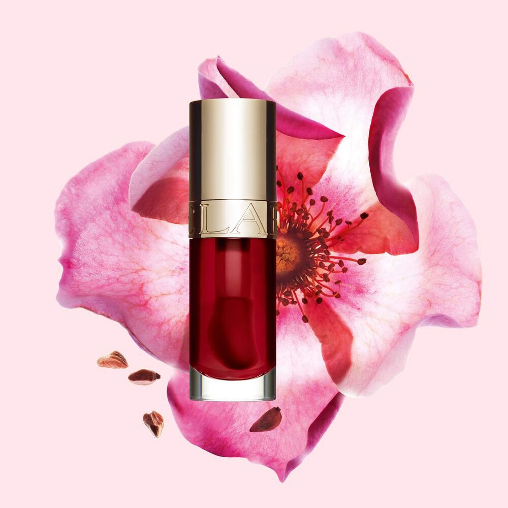 Packshot of Clarins Lip Comfort Oil in Cherry, placed next to a sweetbriar rose on a light pink background.