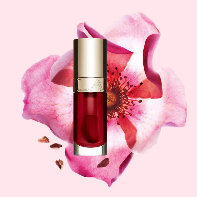 Packshot of Clarins Lip Comfort Oil in Cherry, placed next to a sweetbriar rose on a light pink background.
